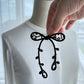 Hand placing the black ribbon brooch onto a white cardigan