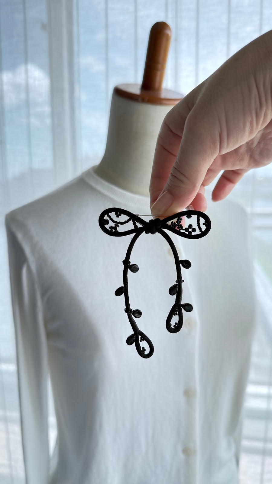 Hand placing the black ribbon brooch onto a white cardigan
