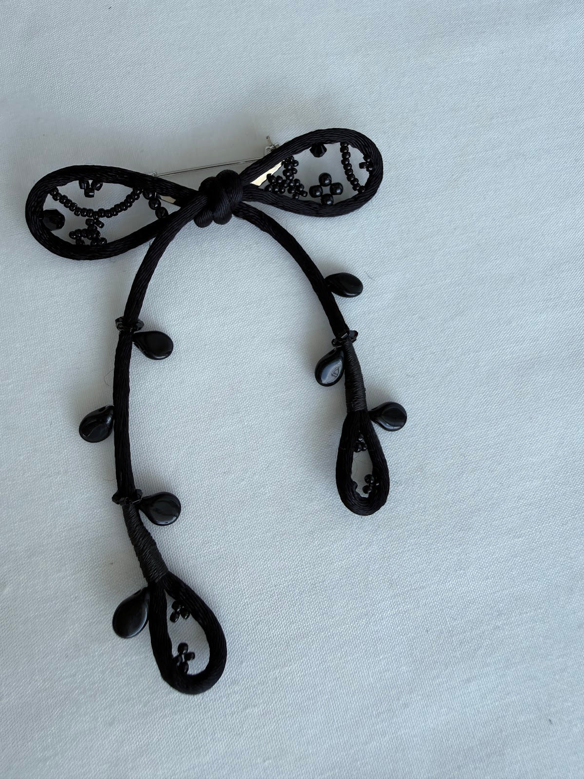Black ribbon brooch close-up showing bead and cord detail