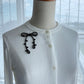 Black ribbon brooch worn on a white cardigan collar