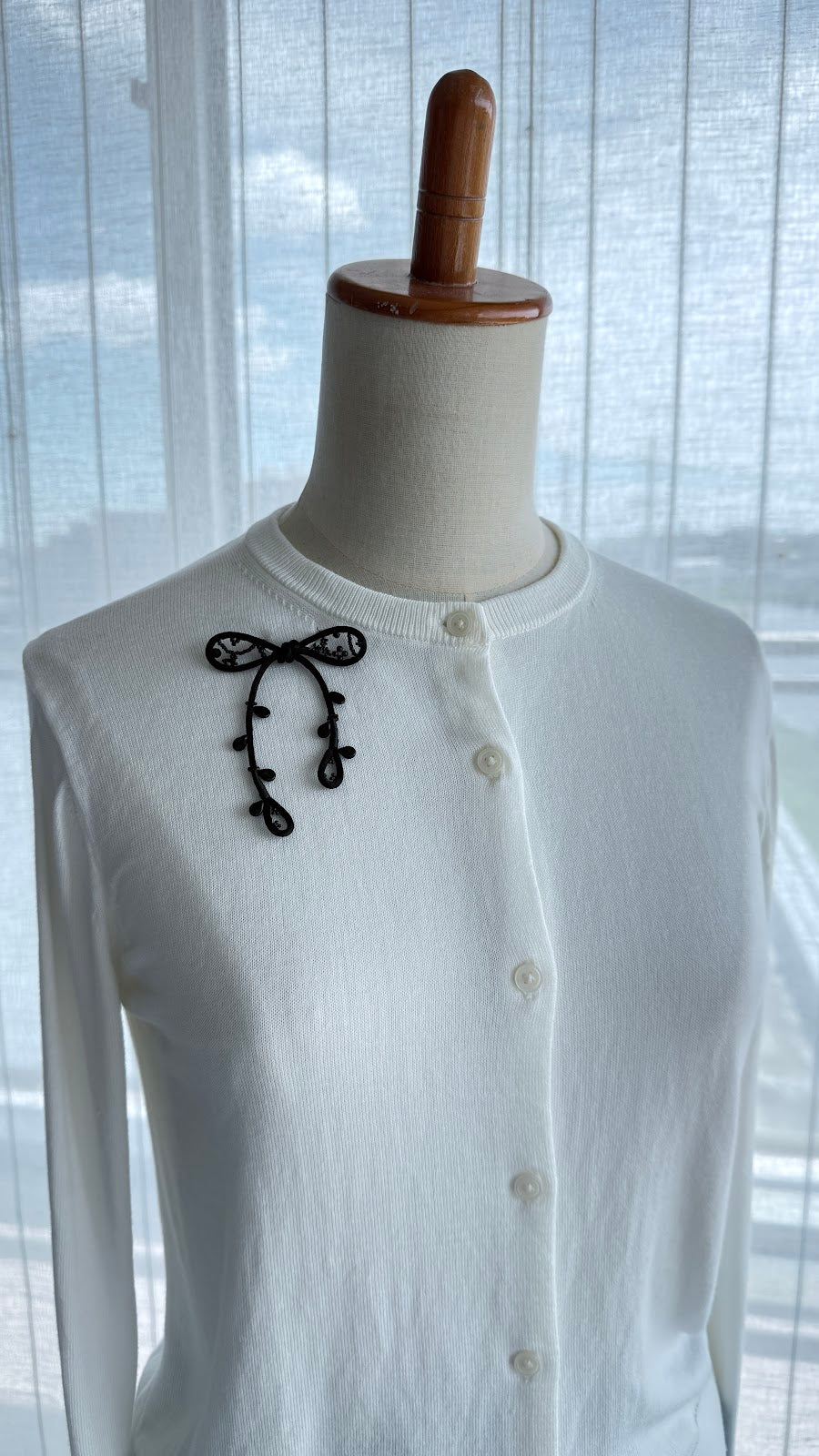 Black ribbon brooch worn on a white cardigan collar